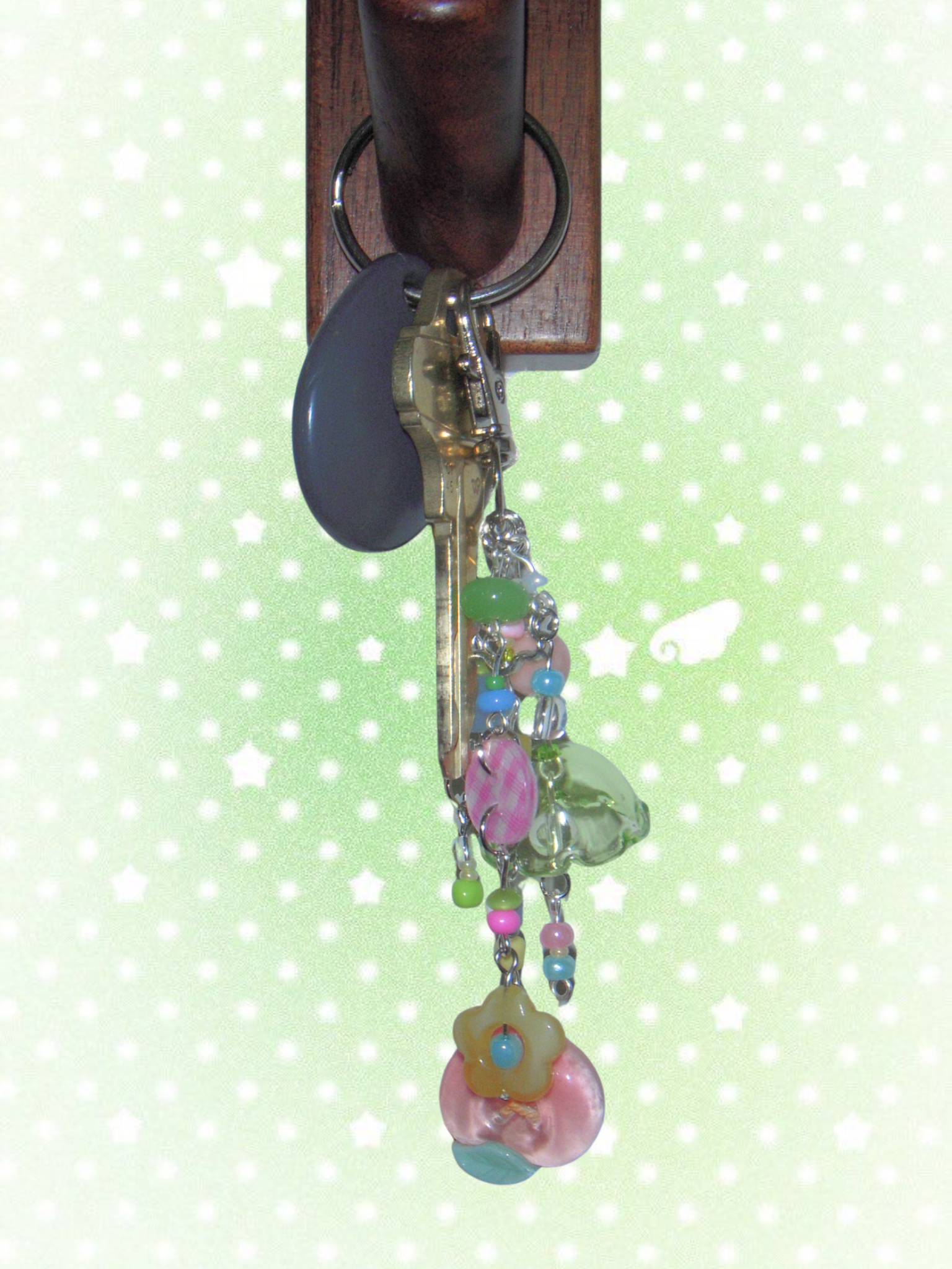 Decorative keychain with colorful beads hanging on a wooden key holder against a light green background.